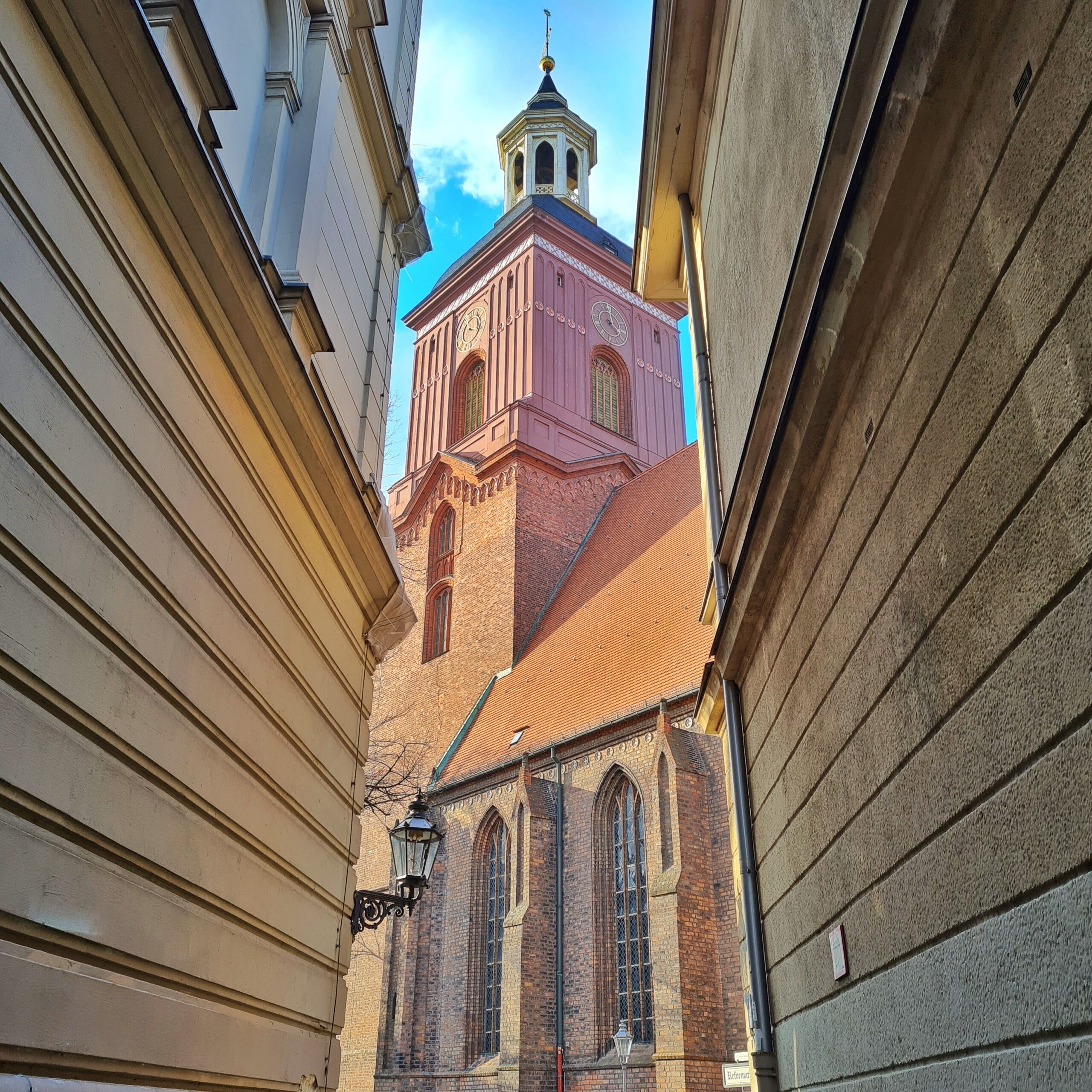 Das Foto ist durch eine schmale Gasse zwischen zwei Hauswänden aufgenommen. Im Hintergrund eine Kirche.