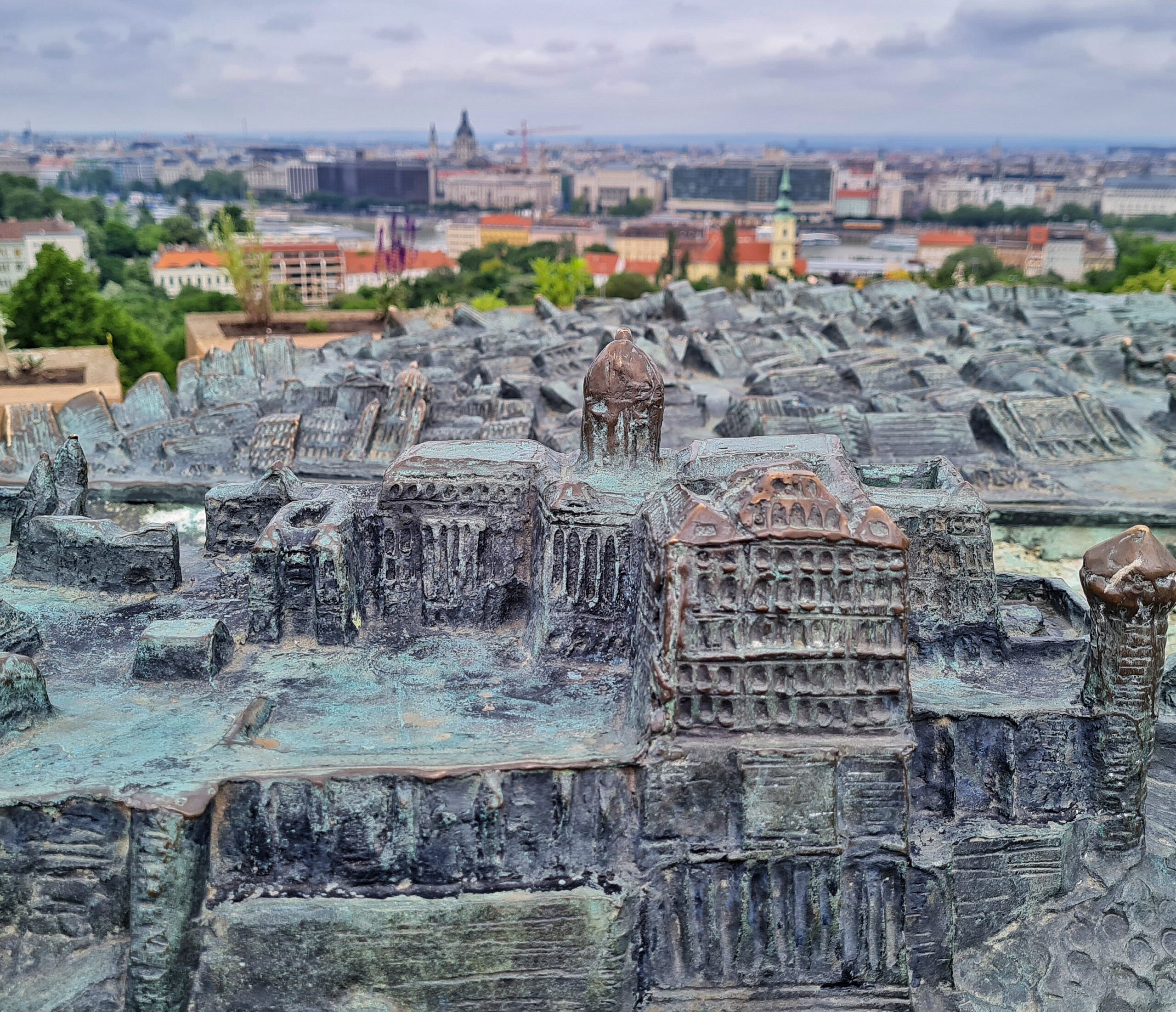 Ein Teil der Grbäude aus Metall aus der Nähe fotografiert. Im Hintergrund sieht man verschwommen echte Gebäude Budapests.