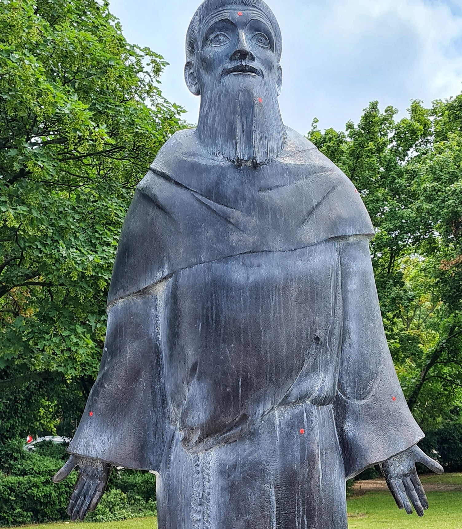 Eine Statue von vorne. Es ist ein Mann mit Bart in einer Mönchskutte. Die Arme hat er nach unten ausgestreckt. Die Handflächen zeigen nach vorn.