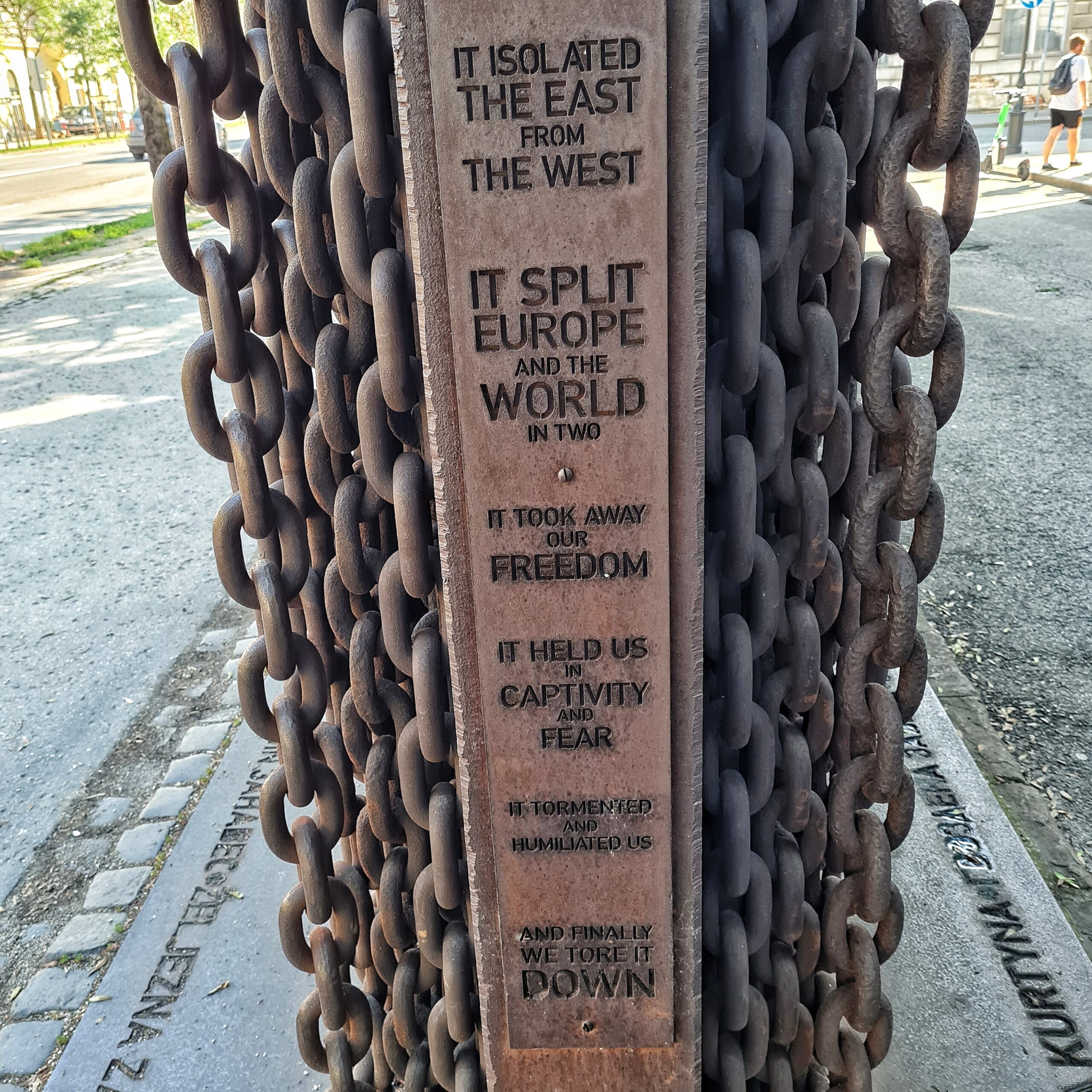 Die gleiche Metallplatte von der Seite fotografiert. Man siejht, dass die Ketten auf beiden Seiten sind. In die Seite ist eingraviert: "It isolated the East from the West", "it split Europe and the World in two", "it took away our Freedom". "It held us in Captavity and Fear". "it tormented and humiliated us", "and finally we tore it down.