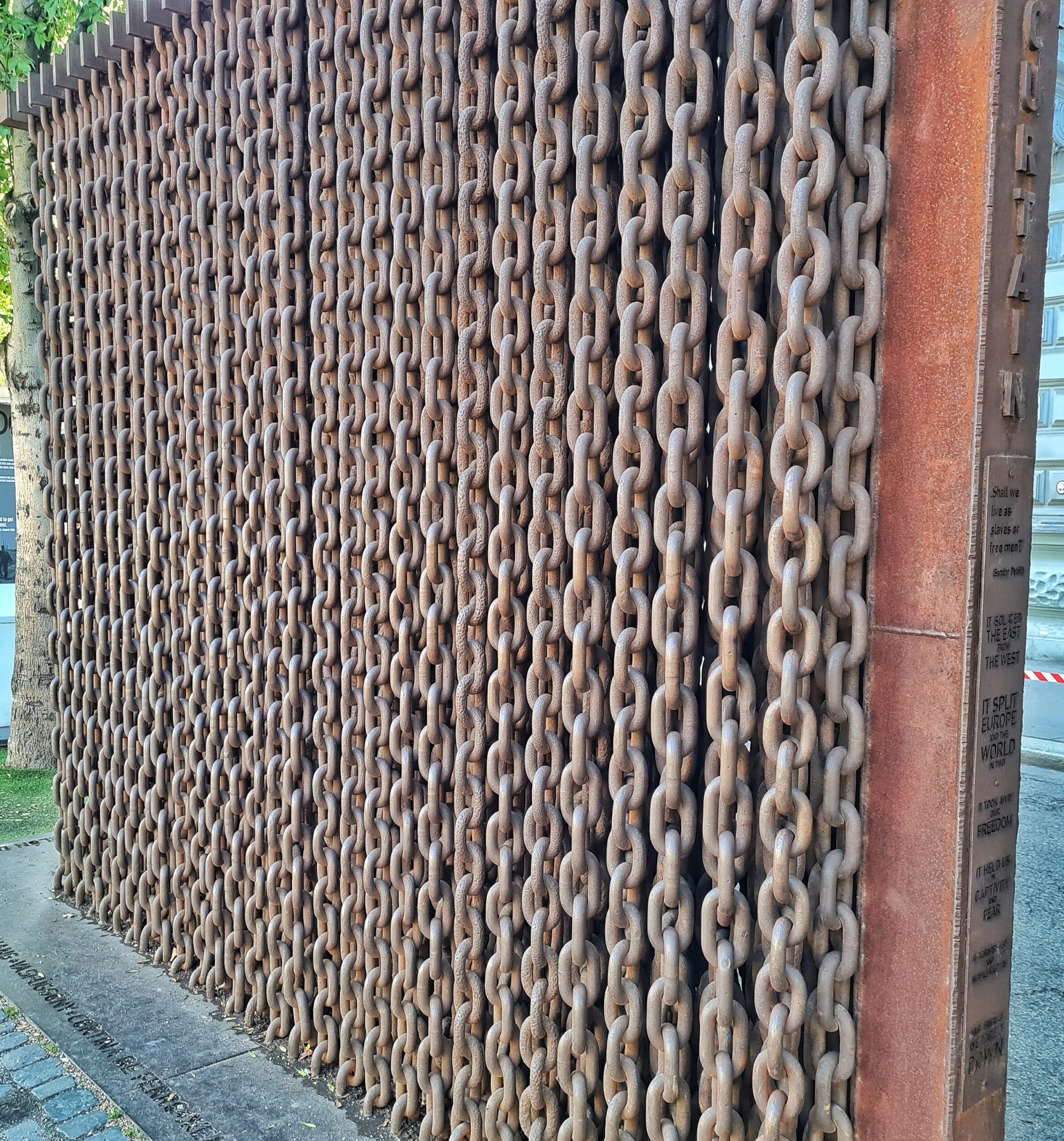 Eine aufrecht stehende große Metallplatte, auf der dicht an dicht Metallketten angebracht sind.