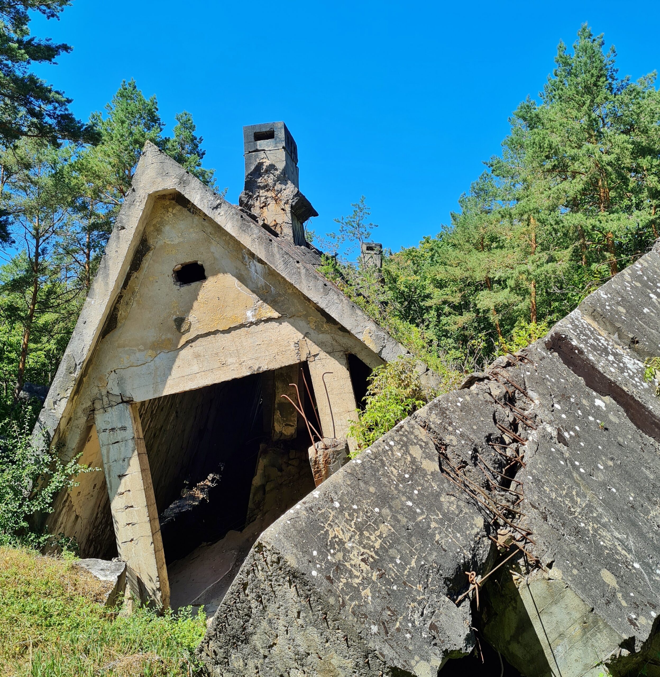Bei diesem zusammengefallenen Gebäude ist recht ein großer massiver Steinblock zu sehen und daneben der obere Teil eines Spitzdaches mkit einem Schornstein.