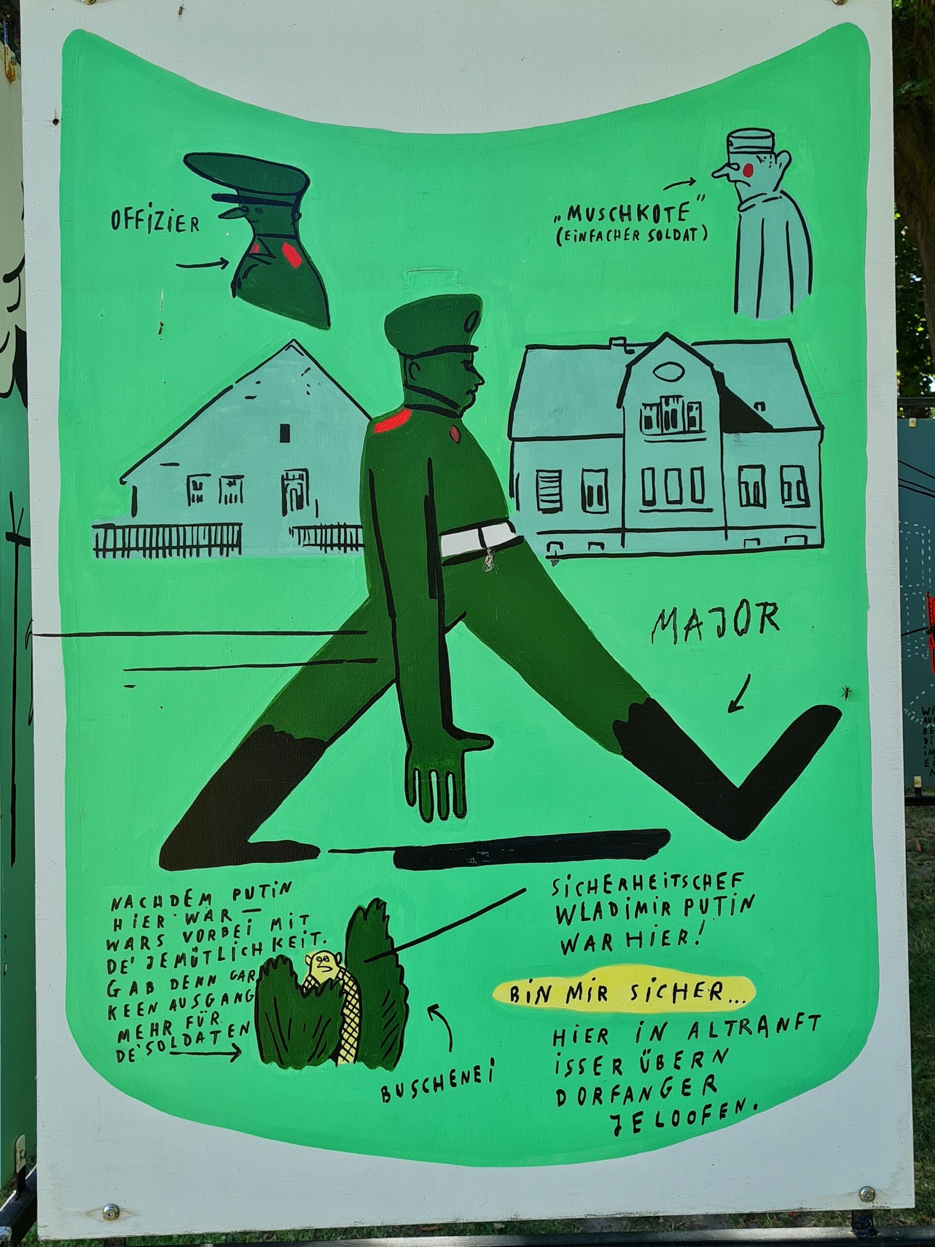 Eine Tafel auf der oben links der Oberkörper eines Mannes in grüner Uniform gezeichnet ist. Daneben steht: Offizier. Rechts die Zeichnung des Oberkörpers eine Mannes in weißer Kleidung und mit einer weißen Mütze. Daneben steht: Muschkote (einfacher Soldat. Darunter sind zwei Häuser gezeichnet, vor denen ein Mann mit einem weit ausholenden Schritt läuft. Er trägt eine grüne Uniform, hat rote Rangabzeichen auf den Schultern, eine weißen Gürtel und schwarze Stiefel. Seine rechte Hand hängt weit herunter. Daneben steht: Major. Darunter die Zeichnung eines Mannes, der sich in grünen Büschen versteckt. Daneben steht: Buschenei. Unten außerdem handschriftliche Texte: Nachdem Putin hier war, wars vorbei mit de Jemütlichkeit. Gab den gar keen Ausgang mehr für de Soldaten. Sicherheitschef Waldimir Putin war hier. Bin mir sicher. Hier in Altranft isser übern Dorfanger jeloofen.