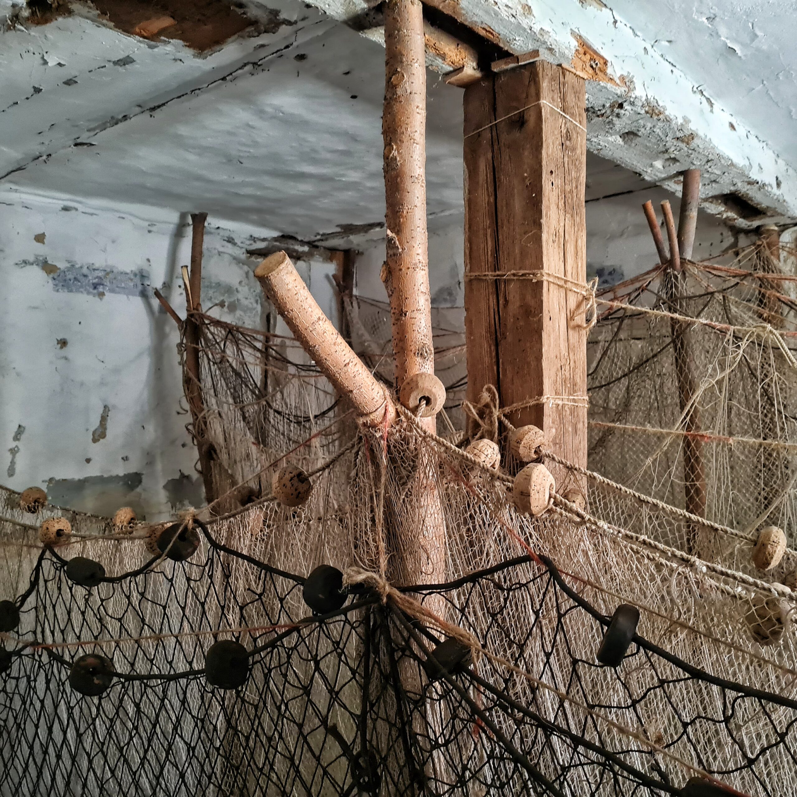 Der obere Teil von Fischernetzen an Holzstangen in einem weiß gestrichenen Raum.