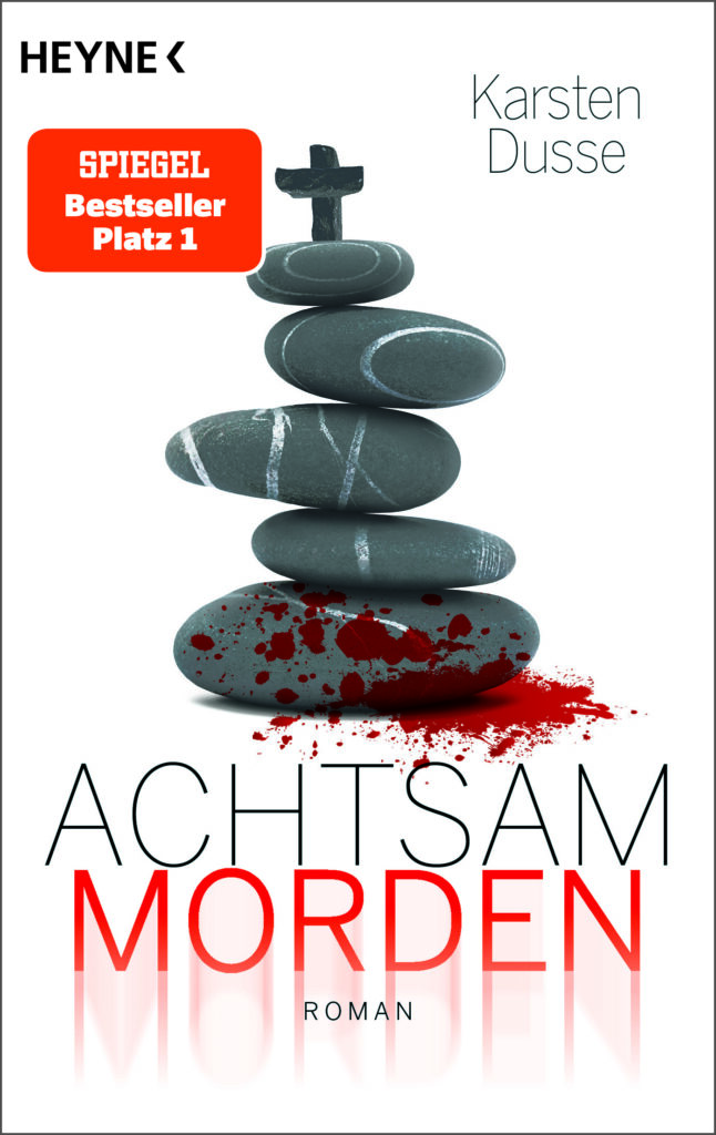 Ein Buchcover. Vor weißem Hintergrund sind mehrere flache, graue Steine übereinandergestapelt. Am unteren Stein ist Blut, auf dem obersten ein kleines Kreuz. Darüber steht der Verlag (Heyne), der Autor (Karsen Dusse) und "Spiegel Bestseller Platz 1".Darunter steht Achtsam Morden. Roman.