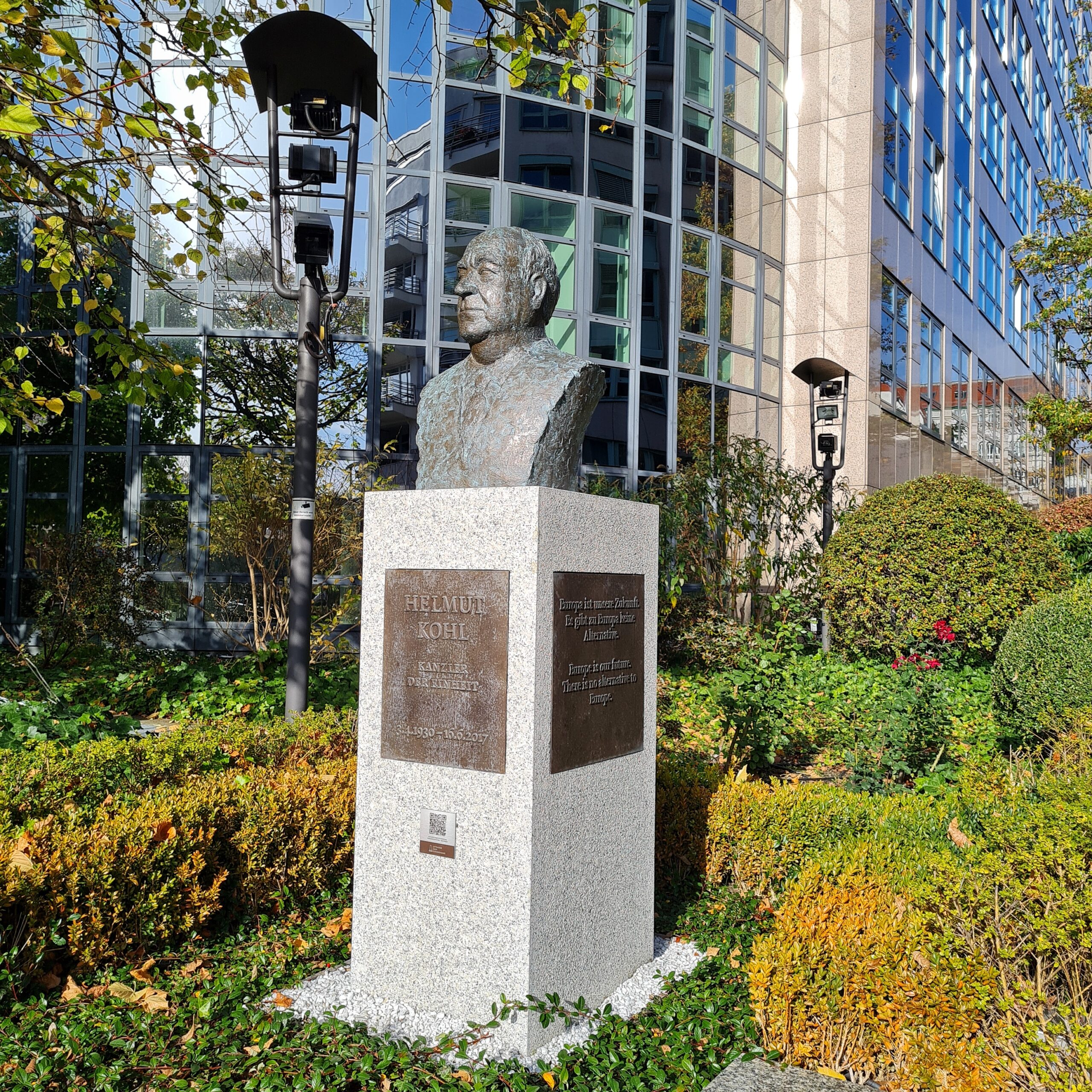Vor einem Glasgebäude inmitten von niedrigen Büschen ein Steinsockel mit der Büste eines Mannes darauf. Auf der Metallplatte darunter steht: Helmut Kohl, Kanzler der Einheit, 3.41930 - 16.6.2017, und auf der seitlichen Metallplatte: Europa ist unsere Zukunft. Es gibt zu Europa keine Alternative.