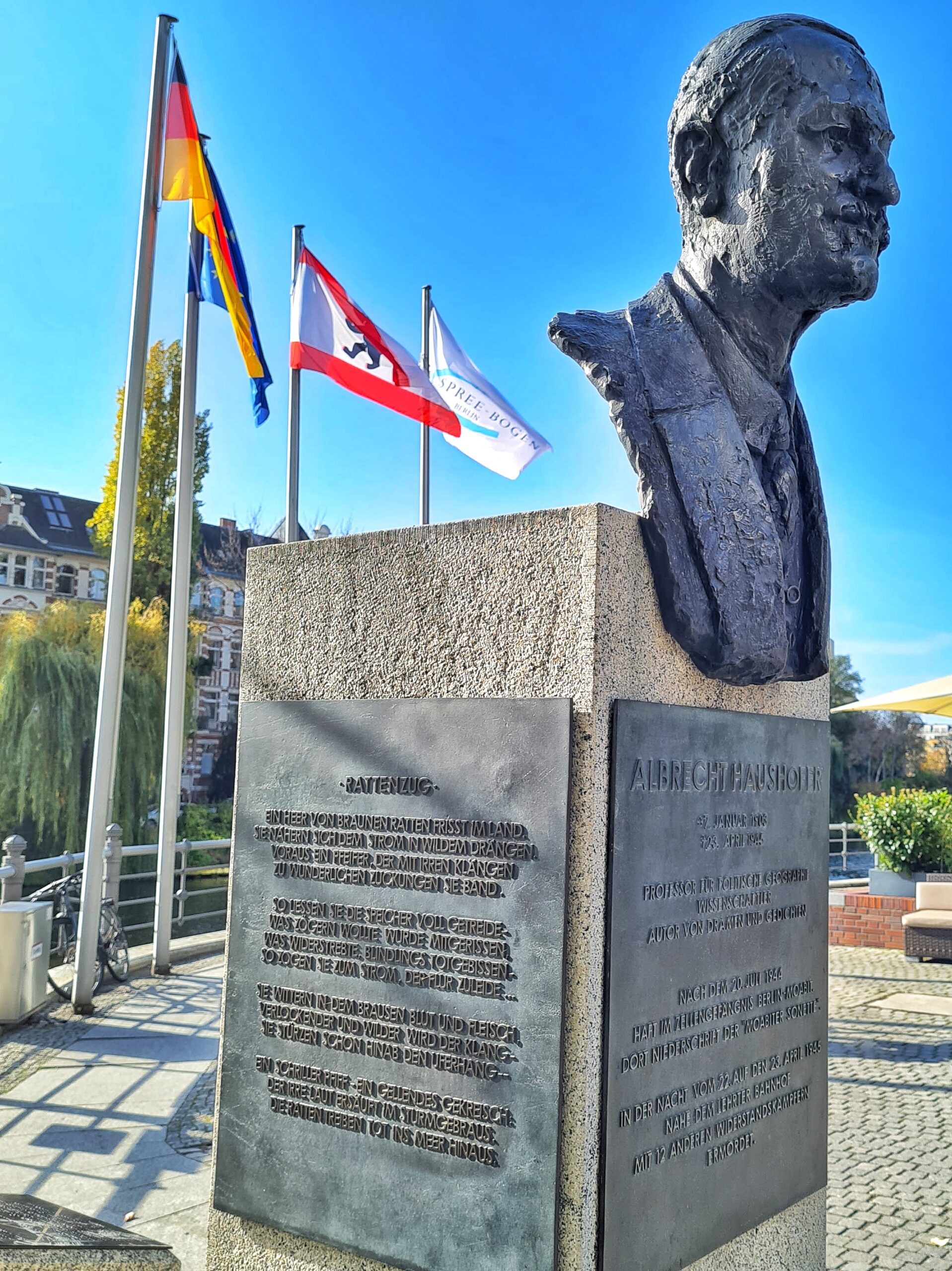 Vorne an einem Steinsockel die Büste eines Mannes. Auf der Metallplatte, die vorne an dem Sockel angebracht ist, kann man den Namen Albrecht Haushofer und biografische Daten zu ihm lesen. Auf der seitlichen Metallplatte ist sein Gedicht "Rattenzug" abgedruckt: Ein Heer von braunen Ratten frisst im Land. Sie nähern sich dem Strom in wildem Drängen. Voraus ein Pfeifer, der mit irren Klängen zu wunderlichen Zuckungen sie band. So ließen sie die Speicher voll Getreide. Was zögern wollte, wurde mitgerissen. Was widerstrebte, blindlings totgebissen. So zogen sie zum Strom, dem Strom zuleide. Sie wittern in dem Brausen Blut und Fleisch. Verlockender und wilder wird der Klang. Sie stürzen schon hinab den Uferhang. Ein schriller Pfiff, ein gellendes Gekreisch. Der irre Laut ersäuft im Sturmgebraus. Die Ratten treiben tot ins Meer hinaus.