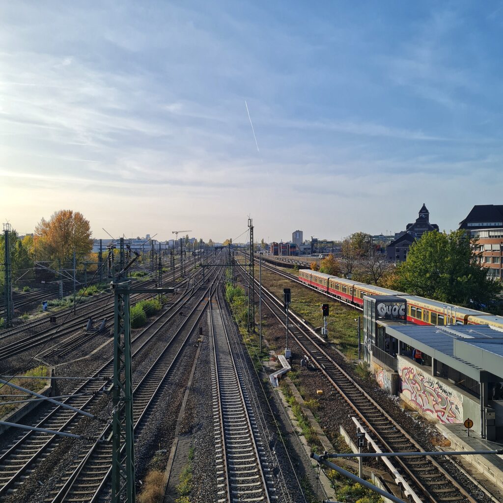 Blick von oben auf acht parallel verlaufende Bahngleise. Zwischen dem ganz recchten Gleis, auf dem eine S-Bahn fährt, und dem Gleis daneben ist ein Teil eines überdachten Bahnsteigs zu sehen.