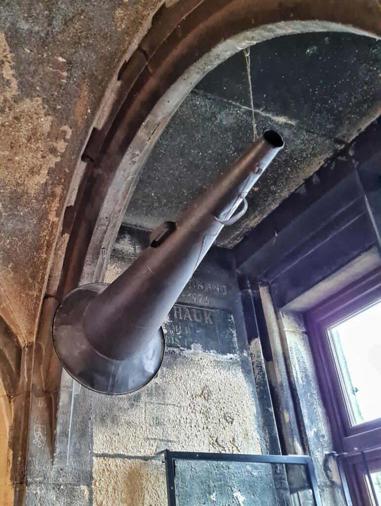 Vor einem Fenster hängt an einem Bogen ein großes Sprachrohr mit einem großen Trichter.