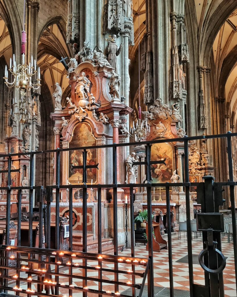 Blick in die Kirche durch ein Absperrgitter im Vordergrund. Man sieht Pfeiler, die mit Gemälden und Figuren reich verziert sind.