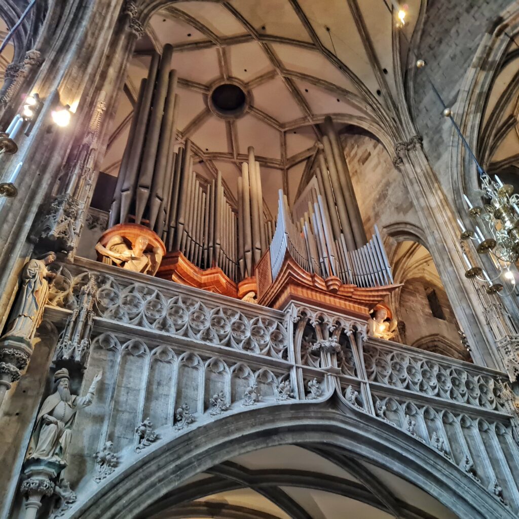 Die Orgel von unten. Der Orgelraum befindet sich auf einem verzierten Metallbogen.