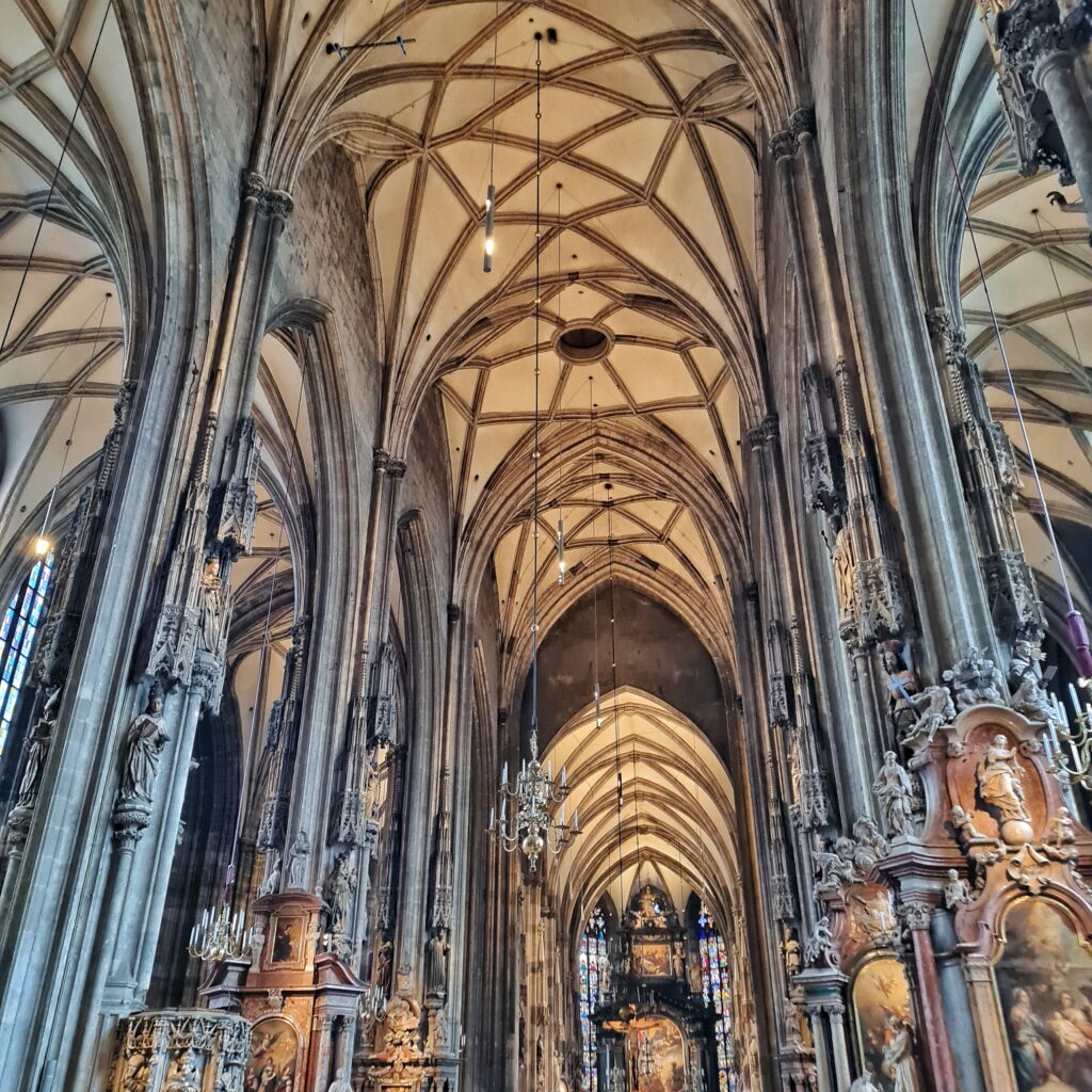 Blick ins Kirchenschiff. Man sieht die Rundbögen und Kuppeln der Decke. Sie sind hell und mit dunklen Bändern eingefasst. Rechts und links sind die Pfeiler und Rundbögen zu den Seitenflügeln zu sehen.