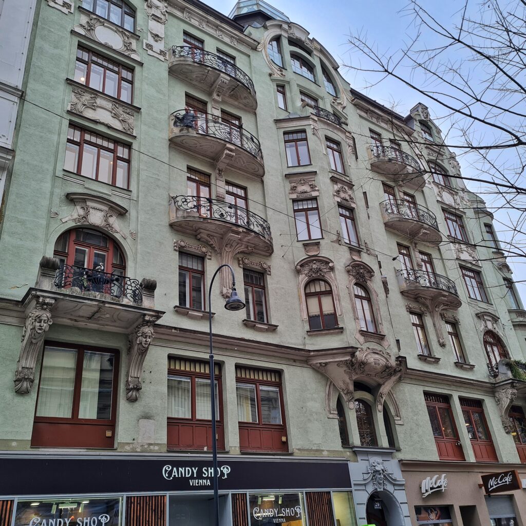 Ein mehrstöckiges hellgrünes Gebäude mit vielen Fenstern, Balkonen und Erkern.